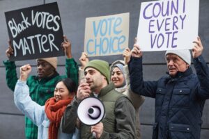 Group of diverse individuals protesting for voting rights with placards and megaphone.
